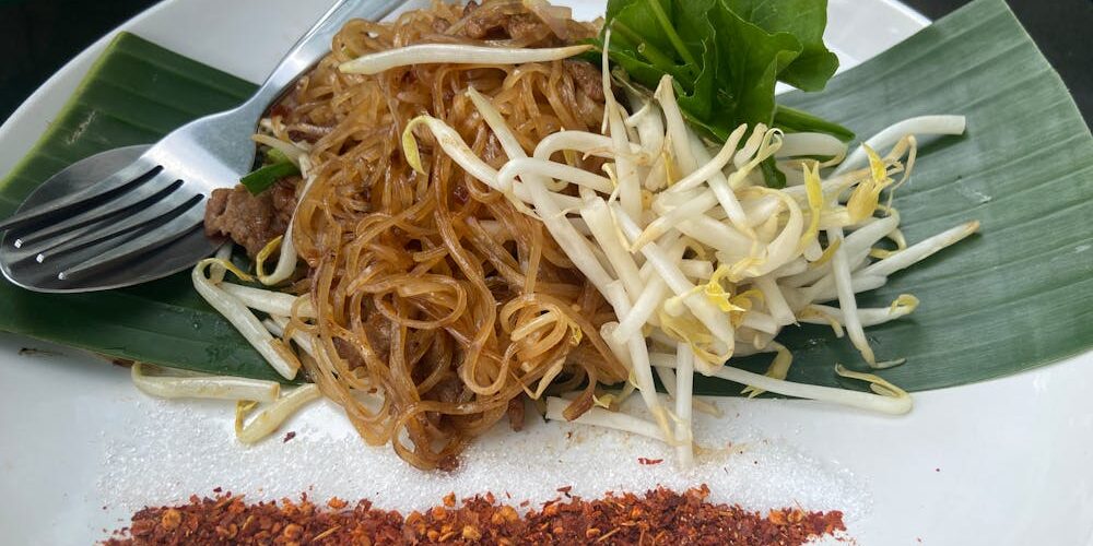 Pad thai servi dans une assiette avec crevettes, cacahuètes et citron vert